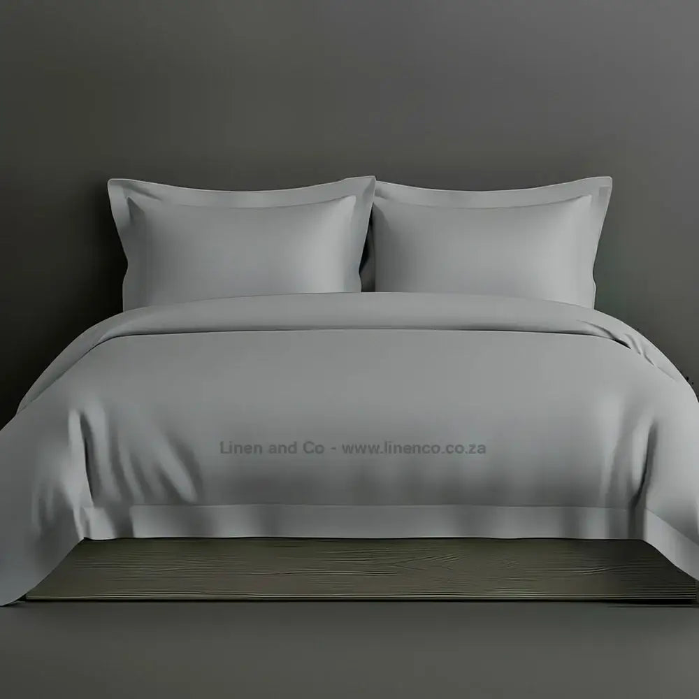 Grey percale duvet cover set with Oxford border from Linen and Co, showcasing elegant hospitality bedding with against a dark grey background.