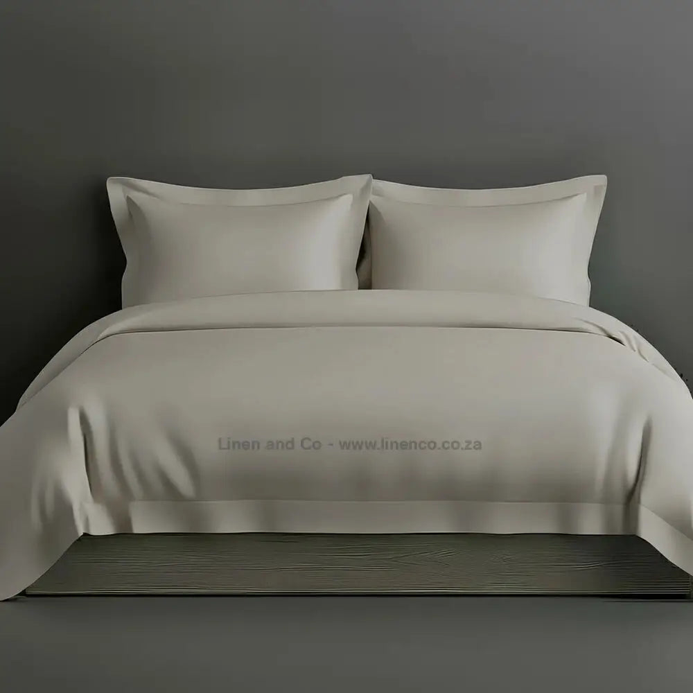 Stone percale duvet cover set with Oxford border from Linen and Co, showcasing elegant hospitality bedding with against a dark grey background.