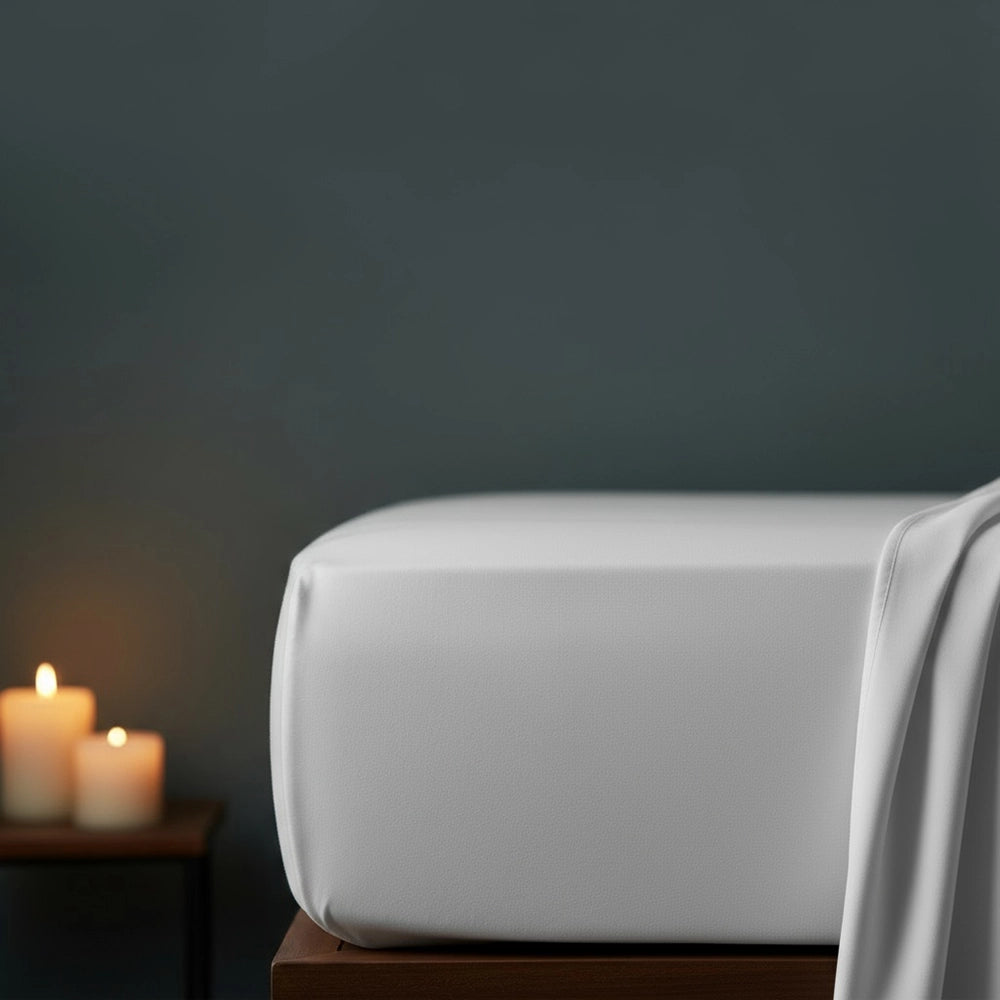 White fitted sheet on bed with candlelight ambiance against moody dark grey wall—premium cotton percale fitted sheet by Linen & Co