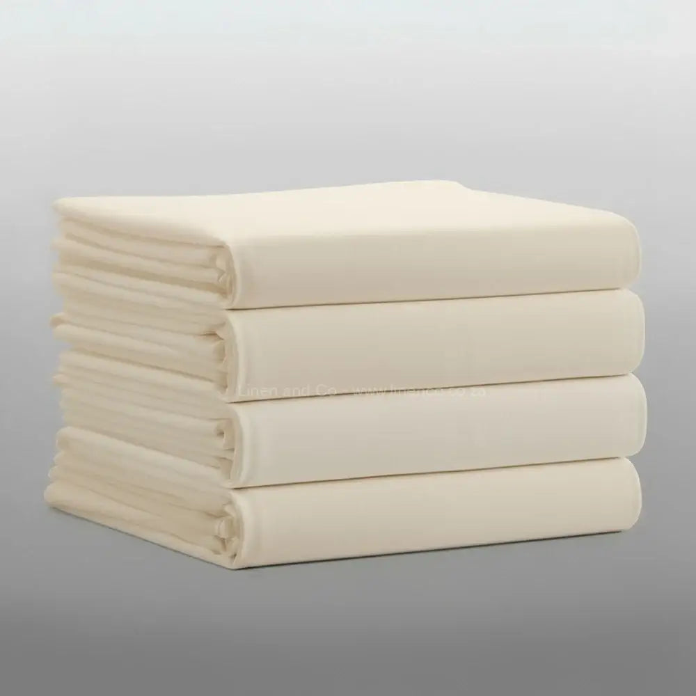 Stack of folded cream percale 200TC flat sheets on light grey background—durable, colour-fast flat sheets by Linen & Co