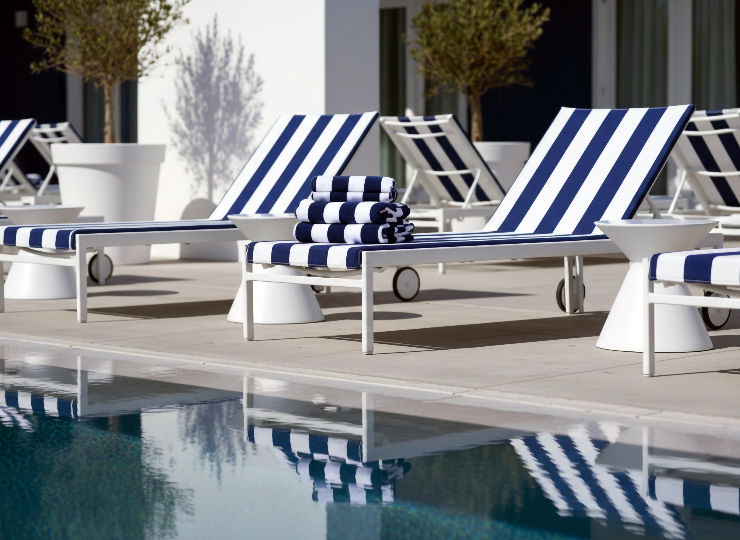 Blue and white striped pool towels stacked on a sun lounger by the poolside at a luxury hotel, by Linen and Co - premium hospitality pool towels