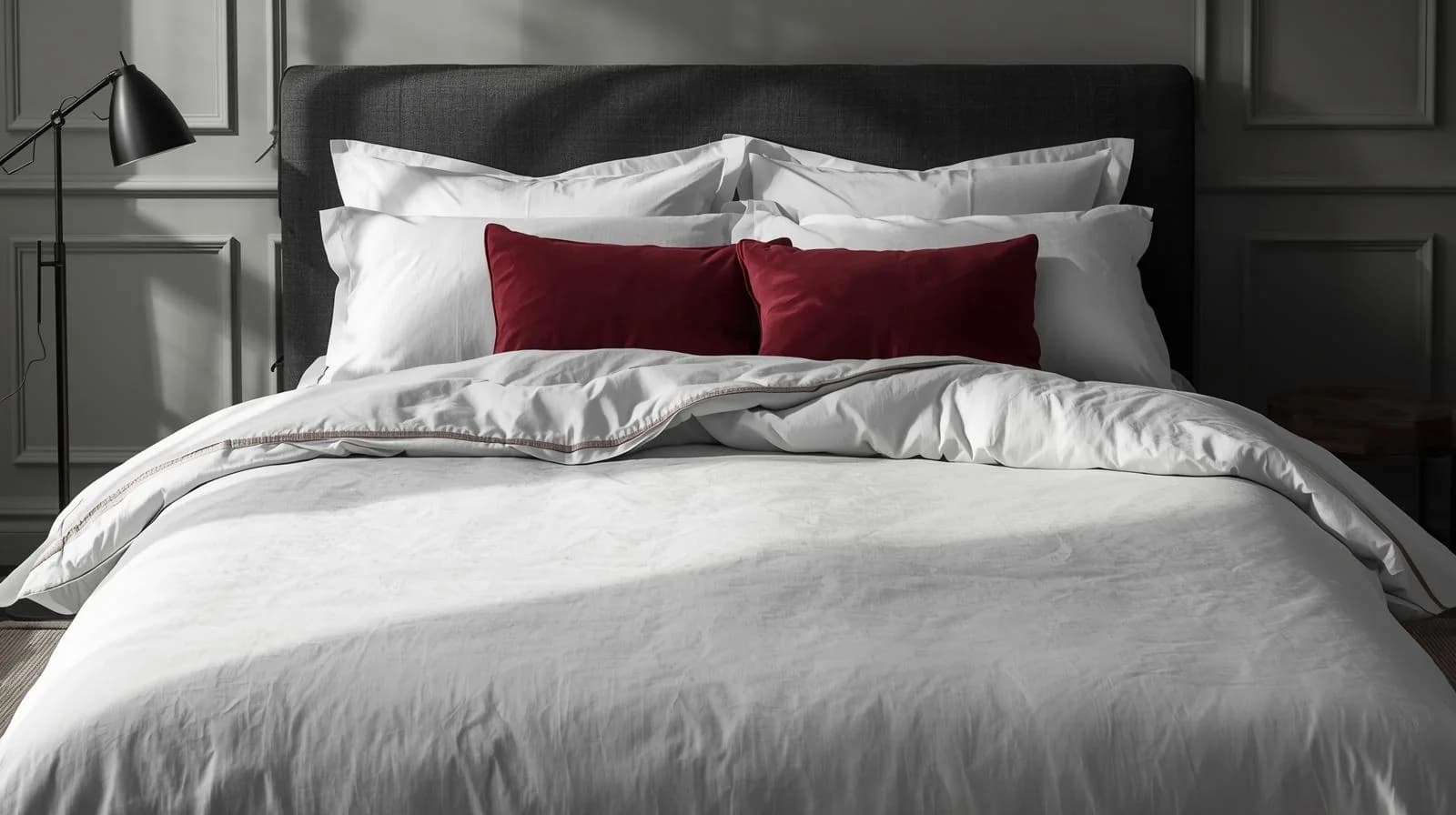 A hotel bed made up in white Linen and Co bed linen with burgundy cushions