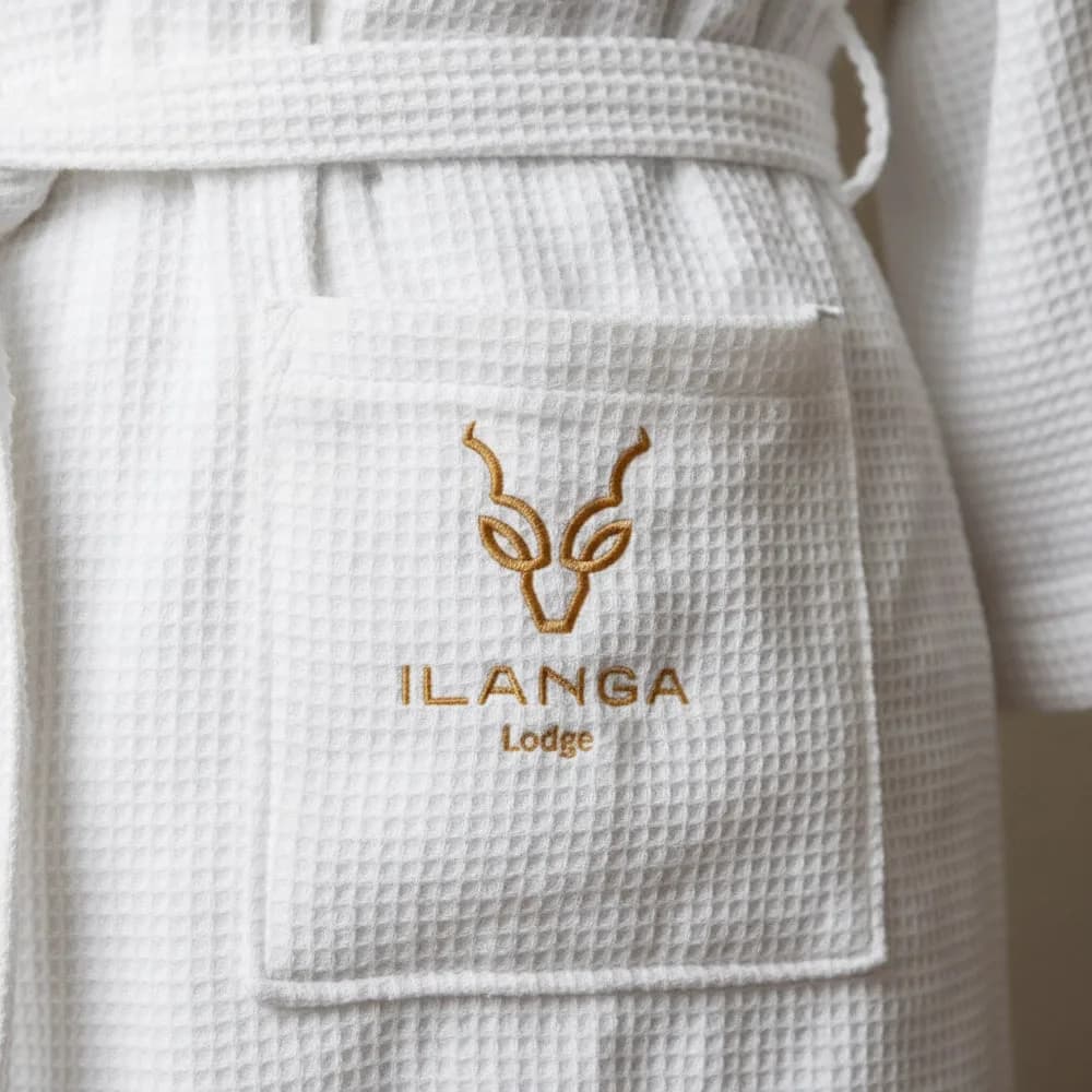 Ilanga Lodge logo embroidered in gold on the pocket of a white waffle weave bathrobe by Linen and Co