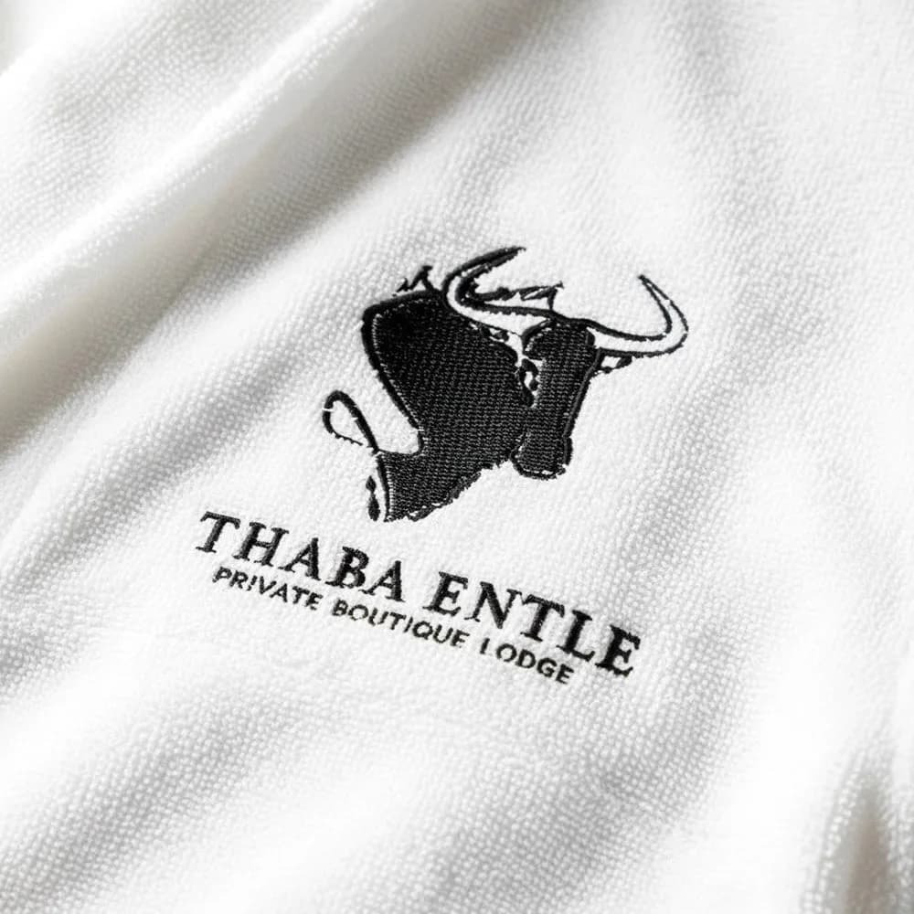 Thaba Entle Private Boutique Lodge logo embroidered in black on a white towelling gown by Linen and Co