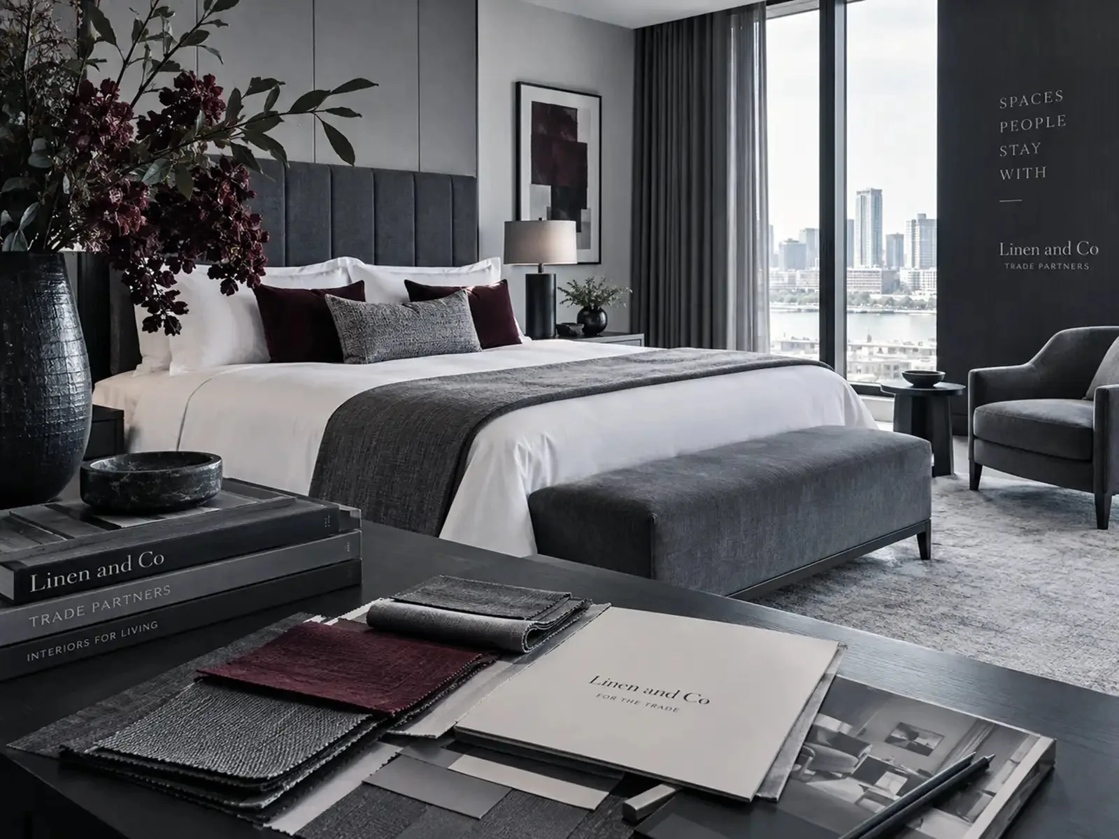A bedroom styled with Linen and Co bed linen, with a Trade Partners welcome pack on the desk
