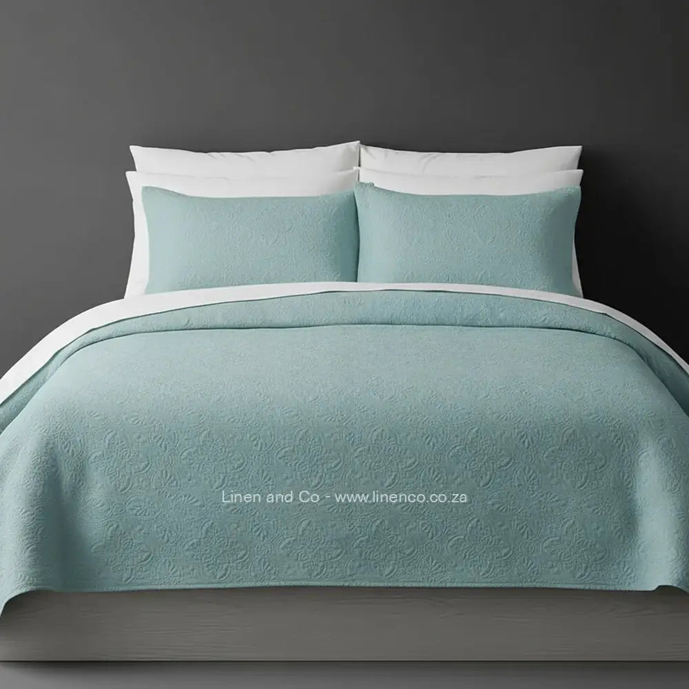 Marine Quilted Bedspread Set with Daisy Design, showcasing textured comforter and matching pillow cases on a bed against a dark grey wall, highlighting professional hospitality textile styling by Linen and Co.