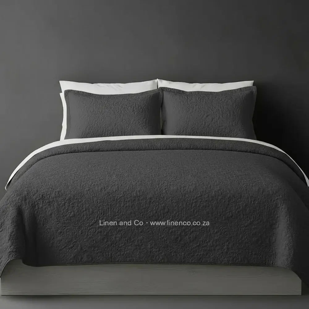 Dark Grey Quilted Bedspread Set with Carmen Design, showcasing textured comforter and matching pillow cases on a bed against a dark grey wall, highlighting professional hospitality textile styling by Linen and Co.