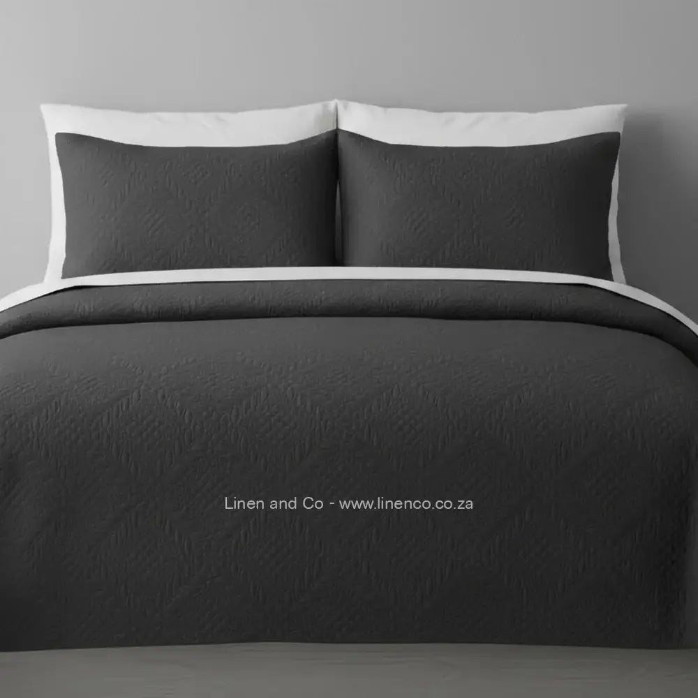 Dark Grey Quilted Bedspread Set with Istanbul Design, showcasing textured comforter and matching pillow cases on a bed against a dark grey wall, highlighting professional hospitality textile styling by Linen and Co