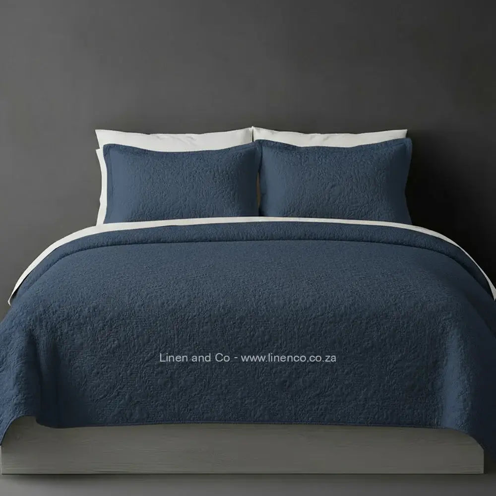 Blue  Quilted Bedspread Set with Carmen Design, showcasing textured comforter and matching pillow cases on a bed against a dark grey wall, highlighting professional hospitality textile styling by Linen and Co.