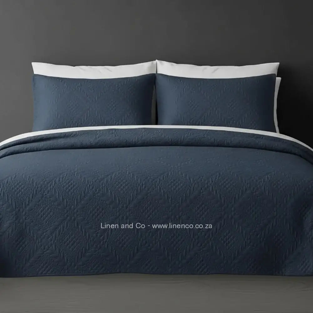 Blue Quilted Bedspread Set with Istanbul Design, showcasing textured comforter and matching pillow cases on a bed against a dark grey wall, highlighting professional hospitality textile styling by Linen and Co.