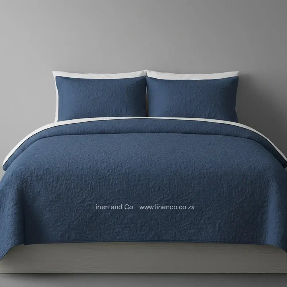 Denim Quilted Bedspread Set with Melissa Design, showcasing textured comforter and matching pillow cases on a bed against a dark grey wall, highlighting professional hospitality textile styling by Linen and Co.