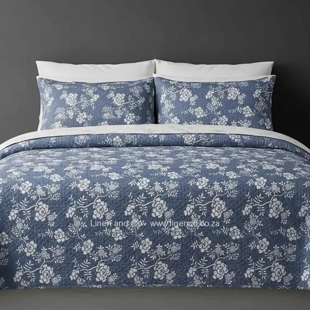 Linen and Co Demin Rochelle Bedspread Set with delicate floral pattern, showcasing quilted comforter and matching pillow cases on a bed against a dark background, highlighting sophisticated hospitality textile design