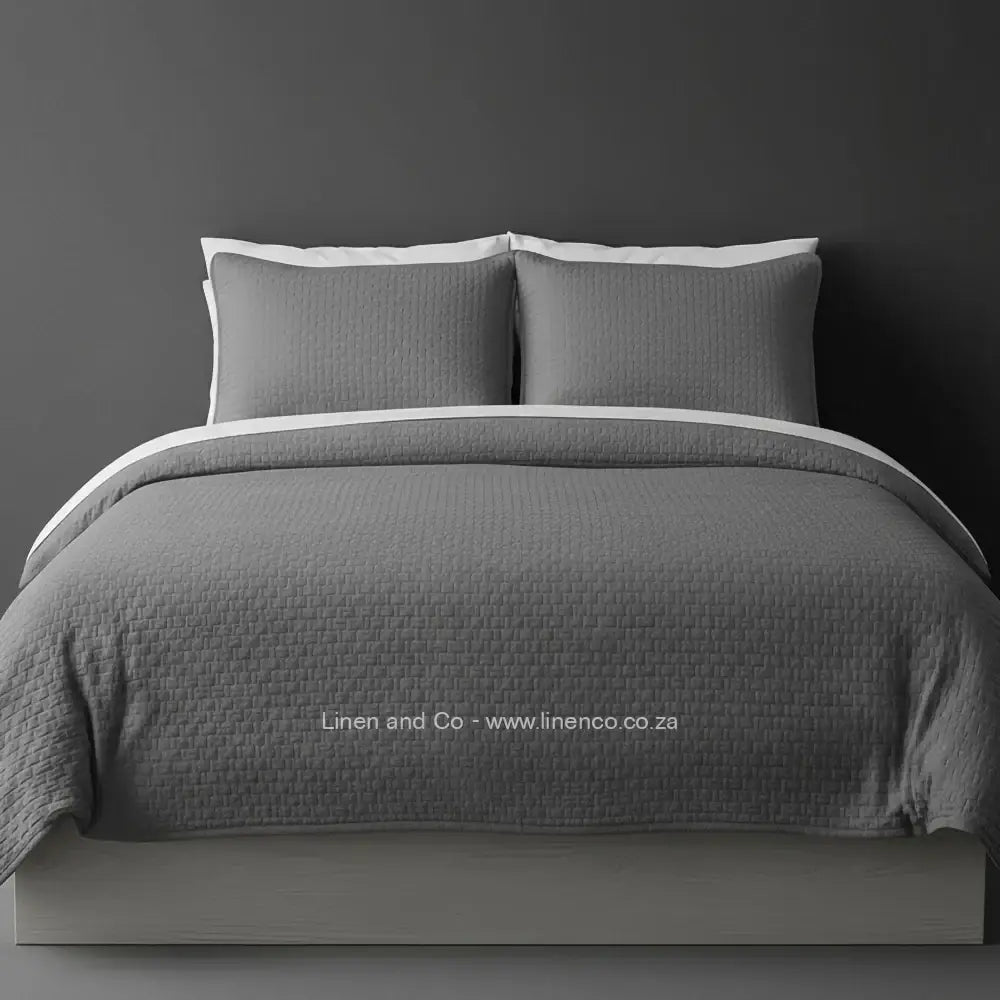Grey Quilted Bedspread Set with Berlin Design, showcasing textured comforter and matching pillow cases on a bed against a dark grey wall, highlighting professional hospitality textile styling by Linen and Co.