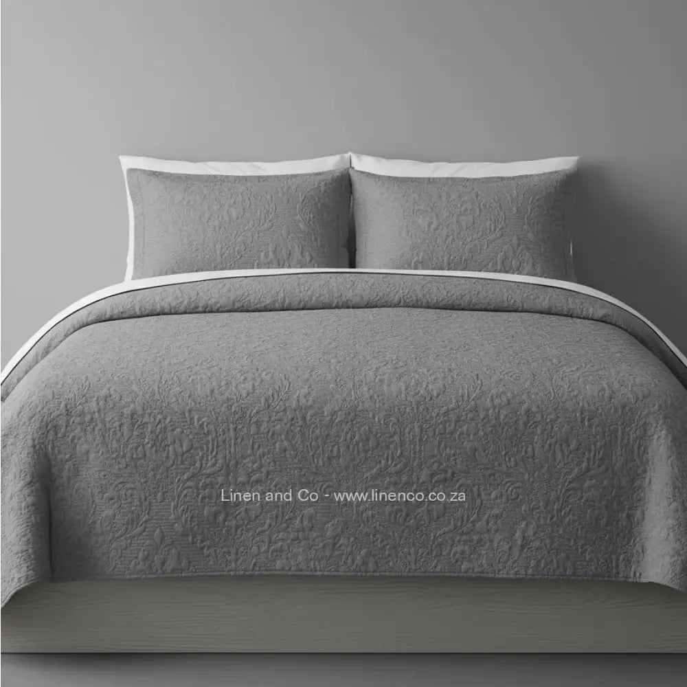 Blue Quilted Bedspread Set with Melissa Design, showcasing textured comforter and matching pillow cases on a bed against a dark grey wall, highlighting professional hospitality textile styling by Linen and Co.