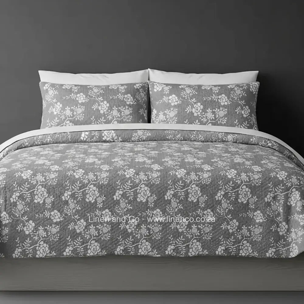 Linen and Co Grey Rochelle Bedspread Set with delicate floral pattern, showcasing quilted comforter and matching pillow cases on a bed against a dark background, highlighting sophisticated hospitality textile design