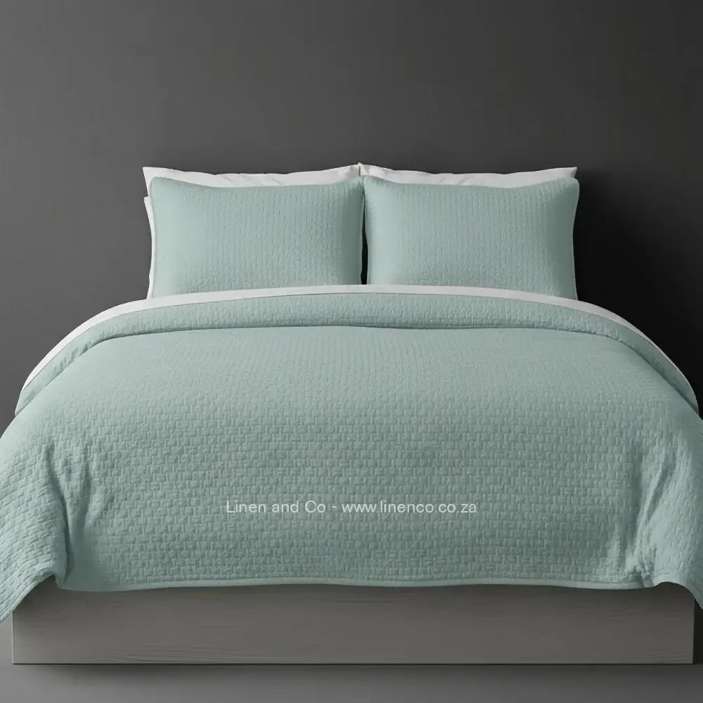 Teal Quilted Bedspread Set with Berlin Design, showcasing textured comforter and matching pillow cases on a bed against a dark grey wall, highlighting professional hospitality textile styling by Linen and Co.