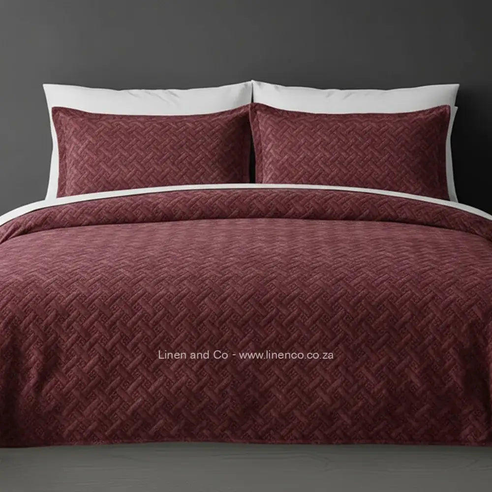 Marroon Quilted Bedspread Set with Italian Velvet, showcasing textured comforter and matching pillow cases on a bed against a dark grey wall, highlighting professional hospitality textile styling by Linen and Co.