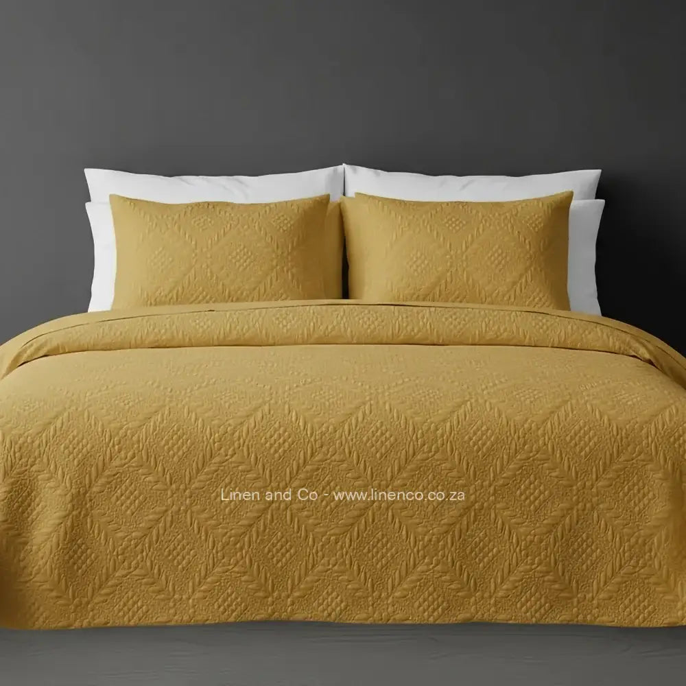 Yellow Mustard Quilted Bedspread Set with Istanbul Design, showcasing textured comforter and matching pillow cases on a bed against a dark grey wall, highlighting professional hospitality textile styling by Linen and Co