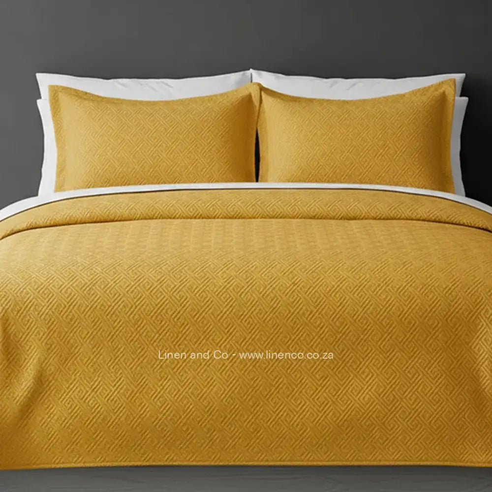 Yellow Mustard Quilted Bedspread Set with Rome Design, showcasing textured comforter and matching pillow cases on a bed against a dark grey wall, highlighting professional hospitality textile styling by Linen and Co.