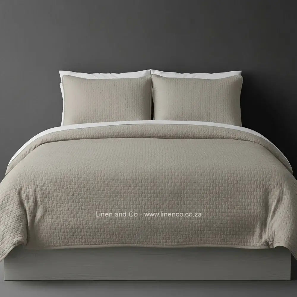 Beige Quilted Bedspread Set with Berlin Design, showcasing textured comforter and matching pillow cases on a bed against a dark grey wall, highlighting professional hospitality textile styling by Linen and Co.