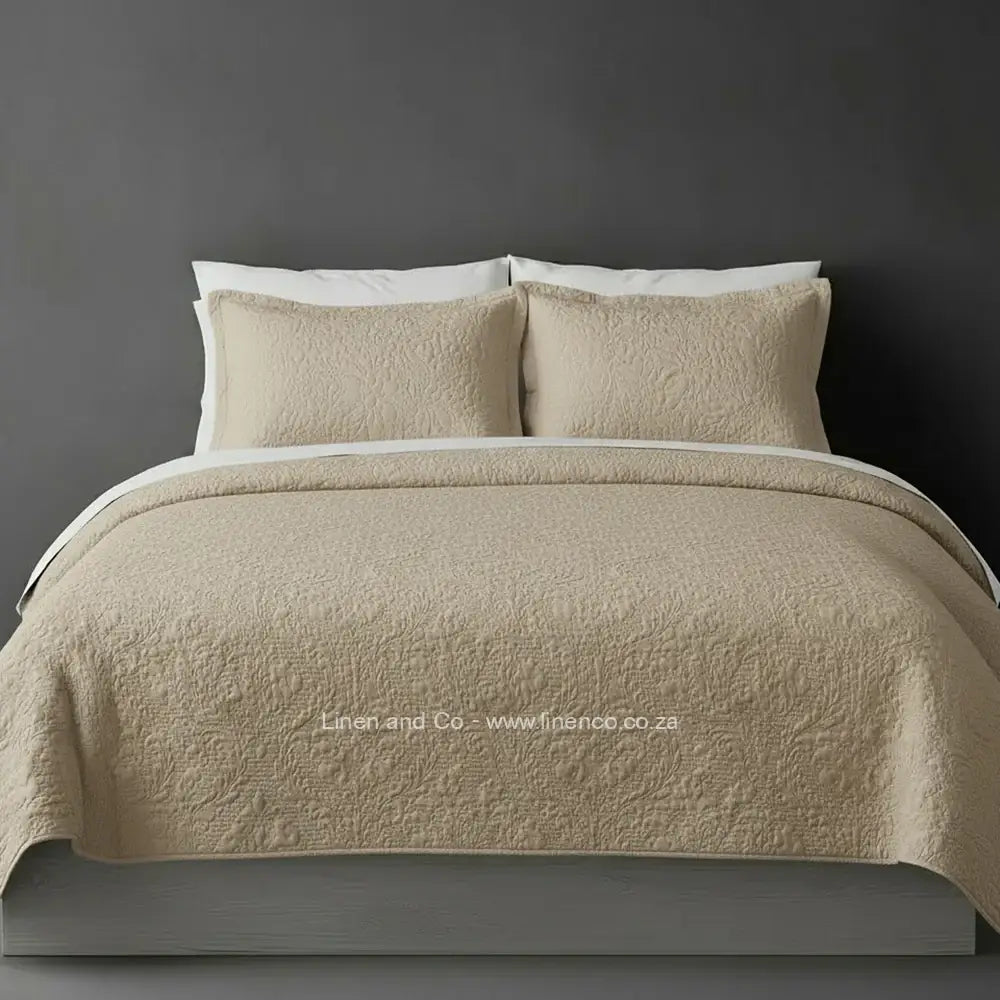 Beige Quilted Bedspread Set with Carmen Design, showcasing textured comforter and matching pillow cases on a bed against a dark grey wall, highlighting professional hospitality textile styling by Linen and Co.