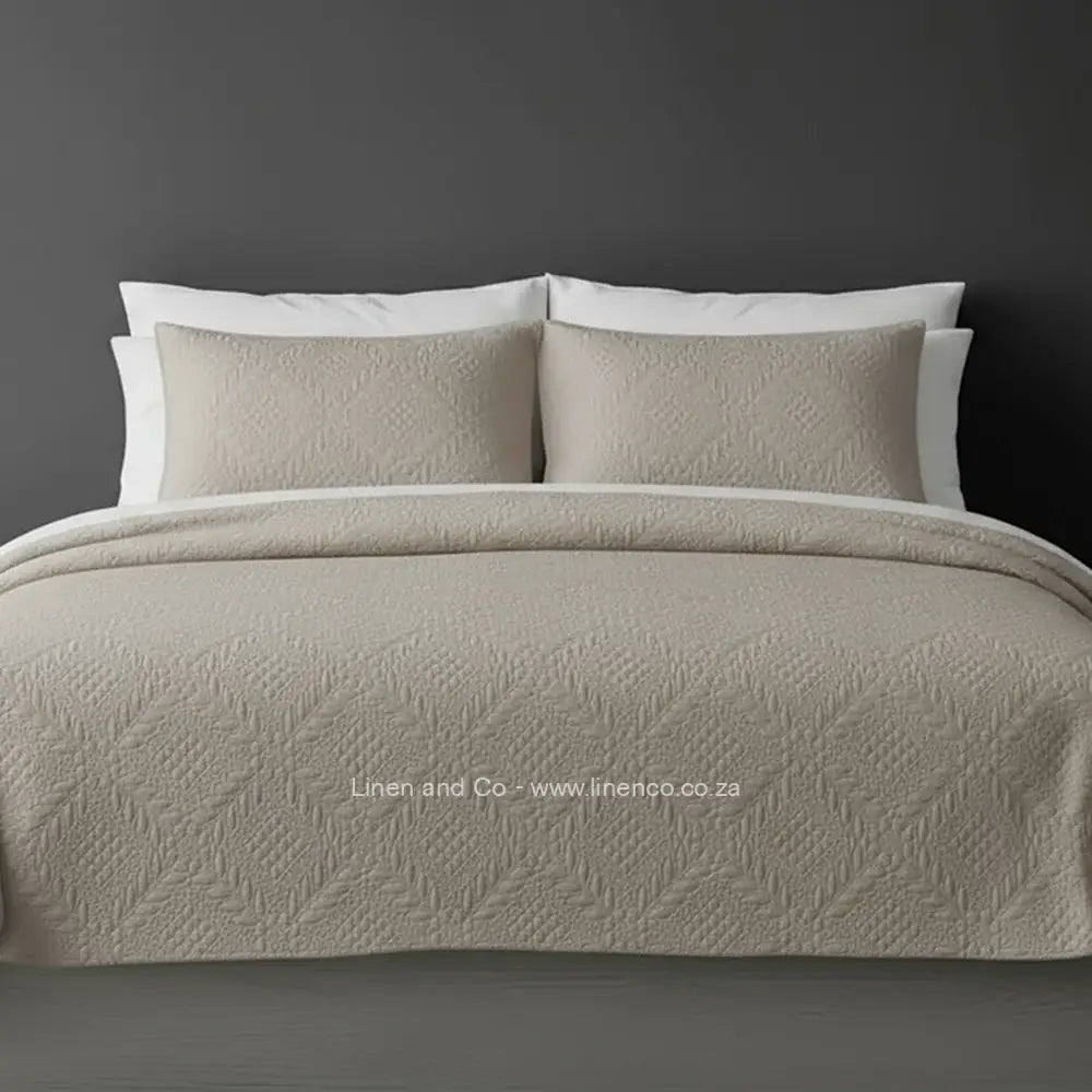 Natural Quilted Bedspread Set with Istanbul Design, showcasing textured comforter and matching pillow cases on a bed against a dark grey wall, highlighting professional hospitality textile styling by Linen and Co.
