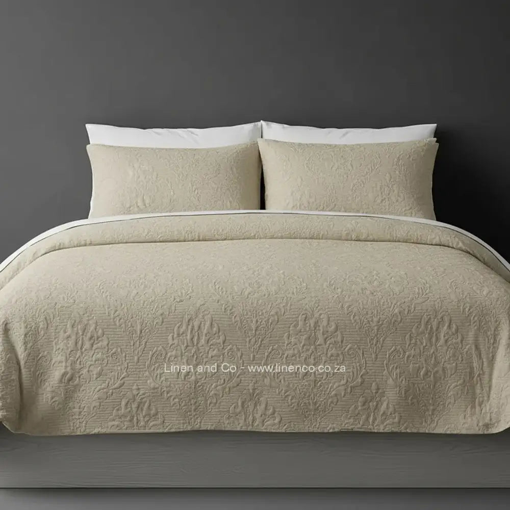 Beige Quilted Bedspread Set with Melissa Design, showcasing textured comforter and matching pillow cases on a bed against a dark grey wall, highlighting professional hospitality textile styling by Linen and Co.