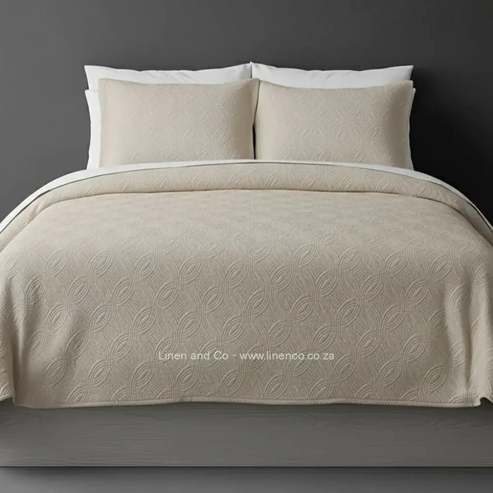 Beige Quilted Bedspread Set with Munich Design, showcasing textured comforter and matching pillow cases on a bed against a dark grey wall, highlighting professional hospitality textile styling by Linen and Co.
