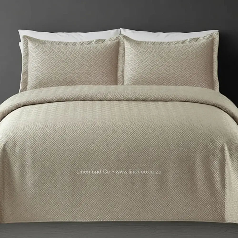 Beige/Natural Quilted Bedspread Set with Rome Design, showcasing textured comforter and matching pillow cases on a bed against a dark grey wall, highlighting professional hospitality textile styling by Linen and Co.