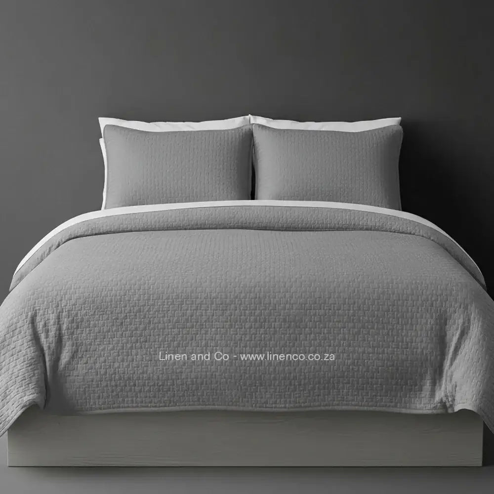 Grey Quilted Bedspread Set with Berlin Design, showcasing textured comforter and matching pillow cases on a bed against a dark grey wall, highlighting professional hospitality textile styling by Linen and Co.