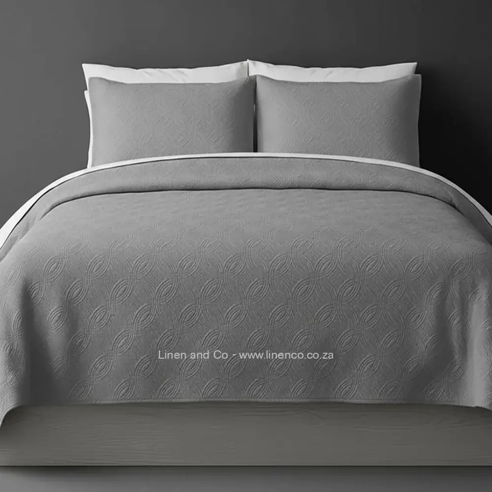 Grey Quilted Bedspread Set with Munich Design, showcasing textured comforter and matching pillow cases on a bed against a dark grey wall, highlighting professional hospitality textile styling by Linen and Co.