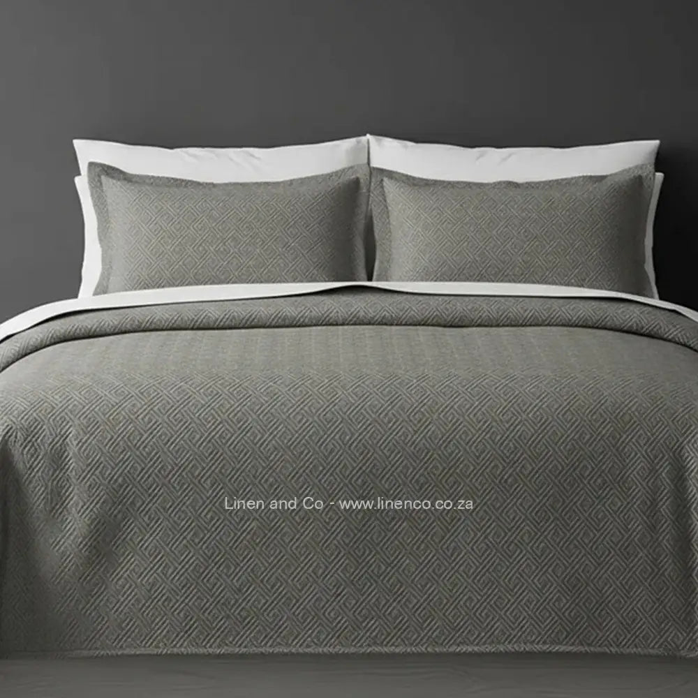 Grey Quilted Bedspread Set with Rome Design, showcasing textured comforter and matching pillow cases on a bed against a dark grey wall, highlighting professional hospitality textile styling by Linen and Co.