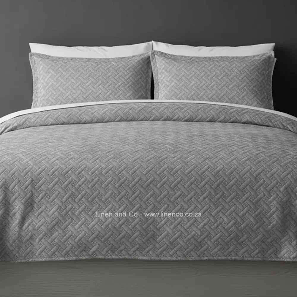 Grey Quilted Bedspread Set with Italian Velvet, showcasing textured comforter and matching pillow cases on a bed against a dark grey wall, highlighting professional hospitality textile styling by Linen and Co.