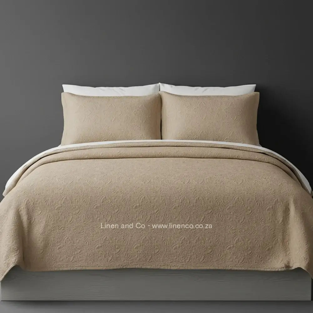 Stone Quilted Bedspread Set with Daisy Design, showcasing textured comforter and matching pillow cases on a bed against a dark grey wall, highlighting professional hospitality textile styling by Linen and Co.