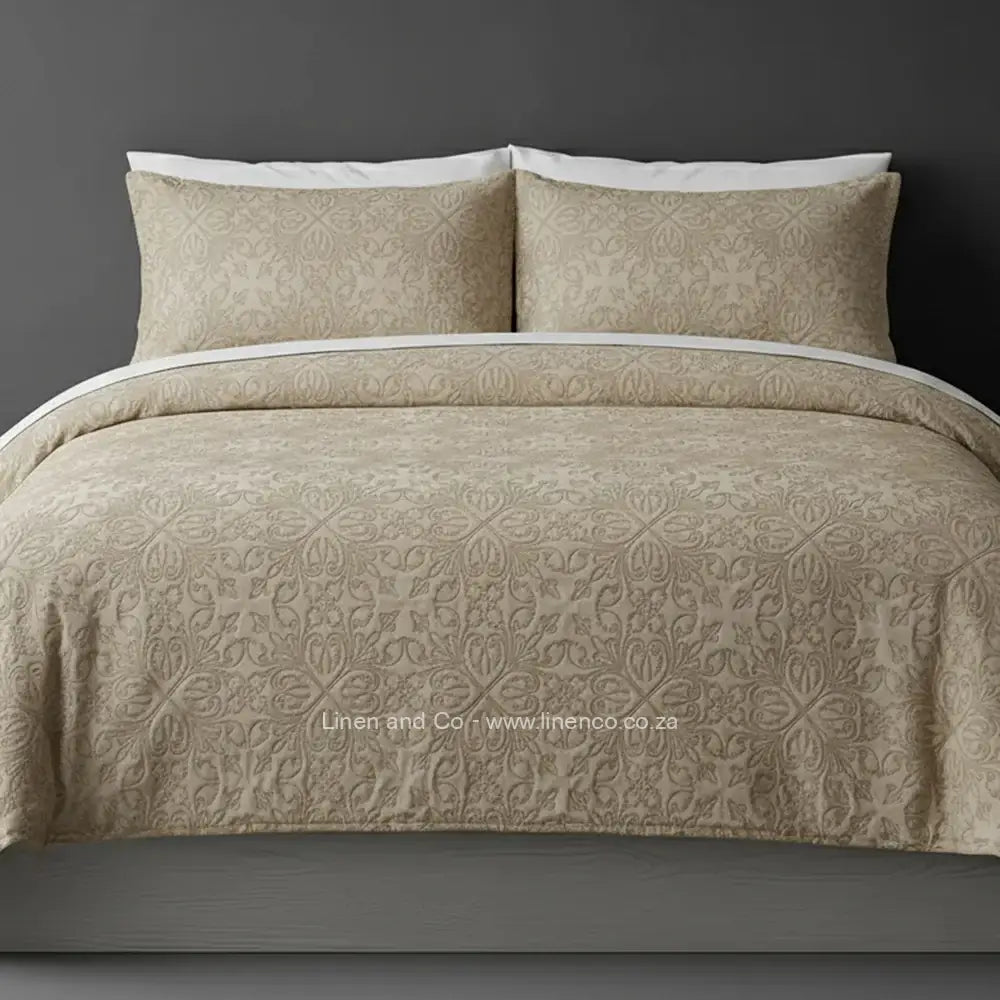 Beige Quilted Bedspread Set with French Velvet, showcasing textured comforter and matching pillow cases on a bed against a dark grey wall, highlighting professional hospitality textile styling by Linen and Co.