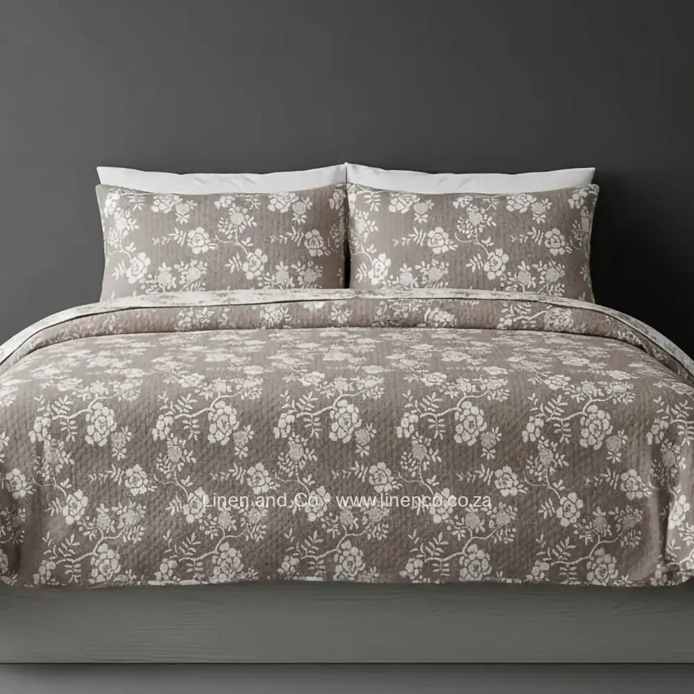 Linen and Co Stone Rochelle Bedspread Set with delicate floral pattern, showcasing quilted comforter and matching pillow cases on a bed against a dark background, highlighting sophisticated hospitality textile design