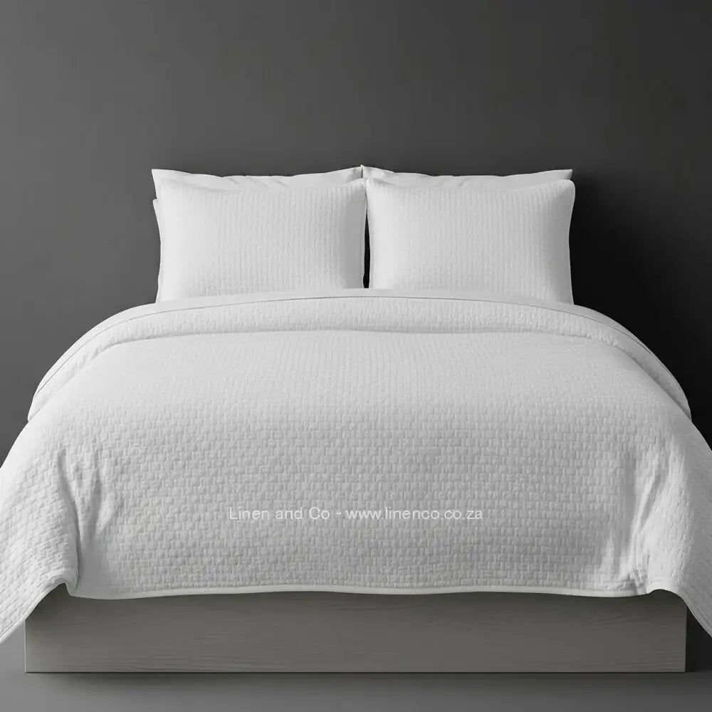 White Quilted Bedspread Set with Berlin Design, showcasing textured comforter and matching pillow cases on a bed against a dark grey wall, highlighting professional hospitality textile styling by Linen and Co.
