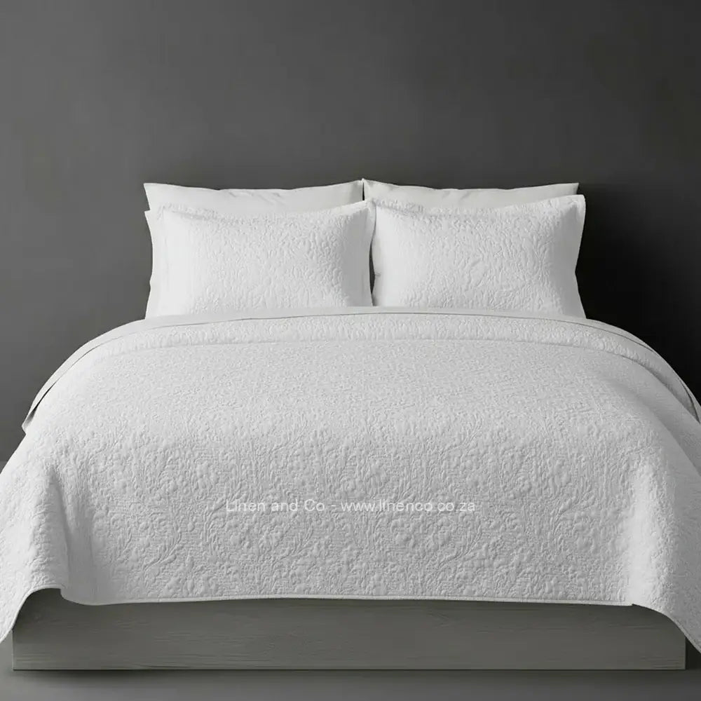 White Quilted Bedspread Set with Carmen Design, showcasing textured comforter and matching pillow cases on a bed against a dark grey wall, highlighting professional hospitality textile styling by Linen and Co.