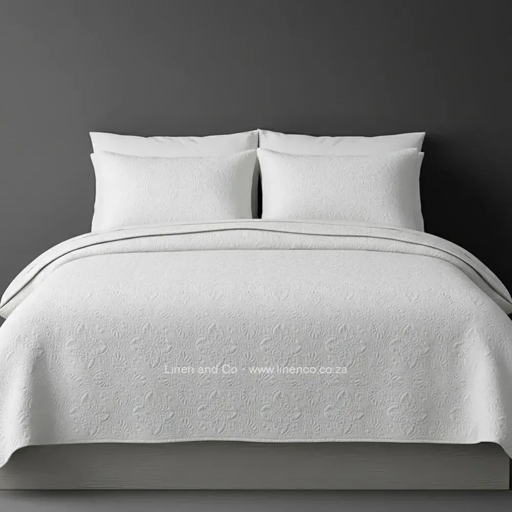 White Quilted Bedspread Set with Daisy Design, showcasing textured comforter and matching pillow cases on a bed against a dark grey wall, highlighting professional hospitality textile styling by Linen and Co.