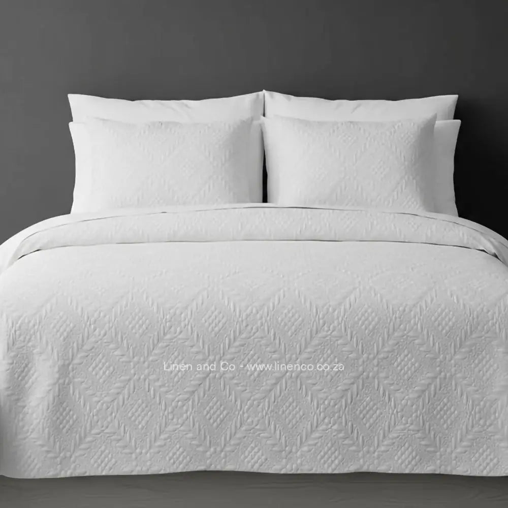 White Quilted Bedspread Set with Istanbul Design, showcasing textured comforter and matching pillow cases on a bed against a dark grey wall, highlighting professional hospitality textile styling by Linen and Co