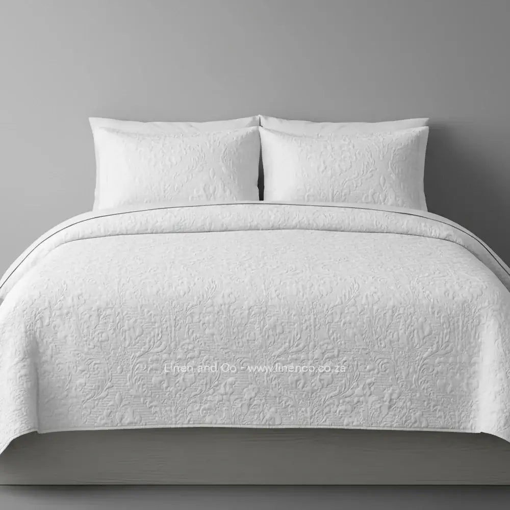 White Quilted Bedspread Set with Melissa Design, showcasing textured comforter and matching pillow cases on a bed against a dark grey wall, highlighting professional hospitality textile styling by Linen and Co.