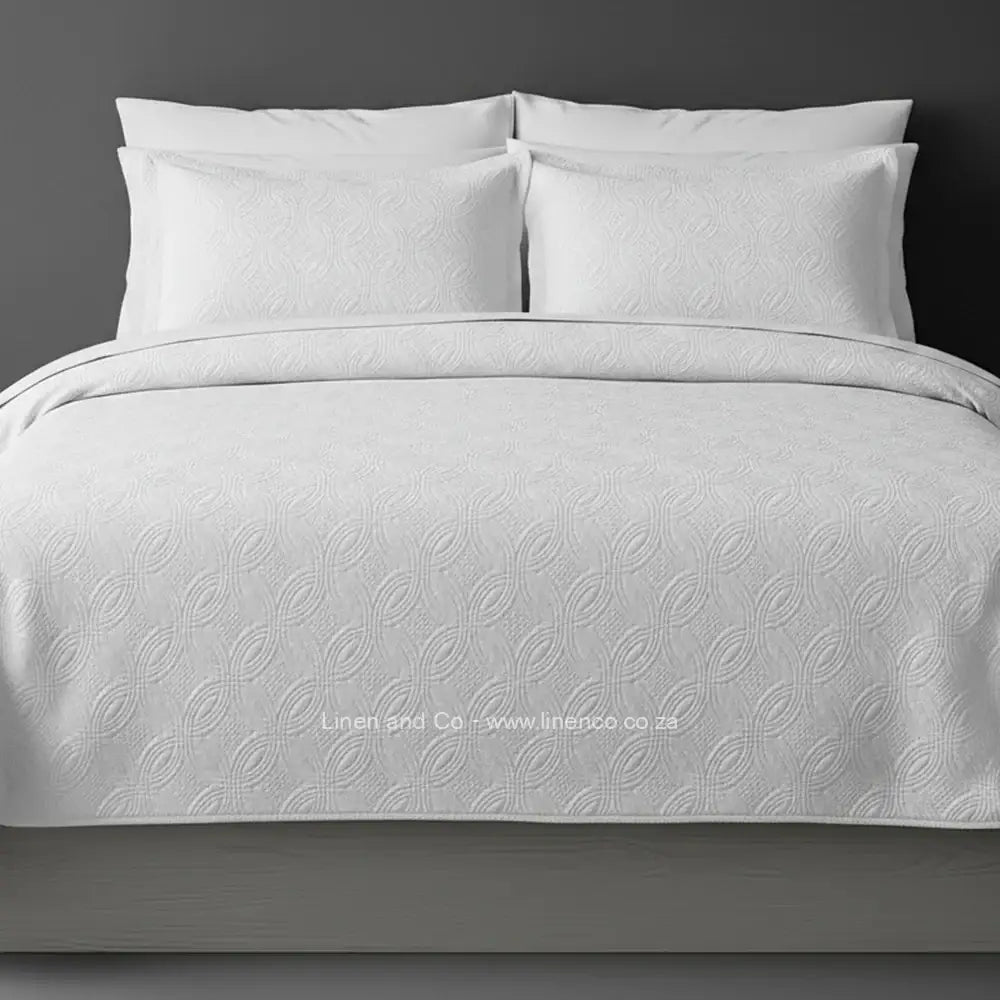 White Quilted Bedspread Set with Munich Design, showcasing textured comforter and matching pillow cases on a bed against a dark grey wall, highlighting professional hospitality textile styling by Linen and Co.
