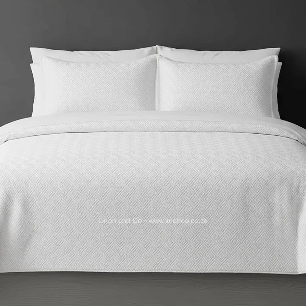 White Quilted Bedspread Set with Rome Design, showcasing textured comforter and matching pillow cases on a bed against a dark grey wall, highlighting professional hospitality textile styling by Linen and Co.
