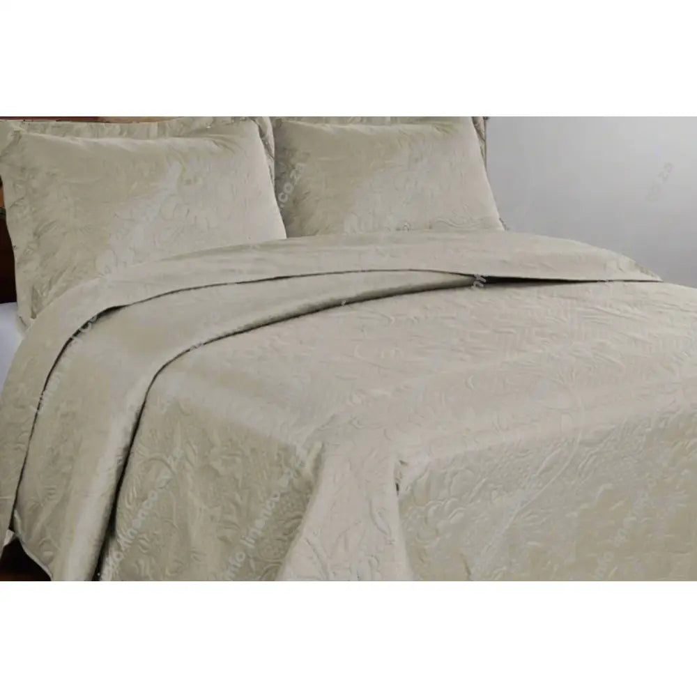 Natural Carmen Design textured bedspread on a bed with matching pillows in a bedroom setting.