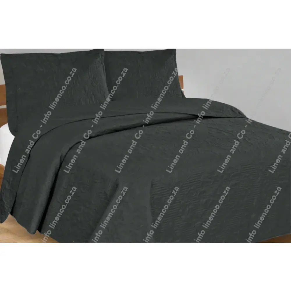 Charcoal Grey Melissa Design textured quilt and pillow set on a bed in a bedroom setting.