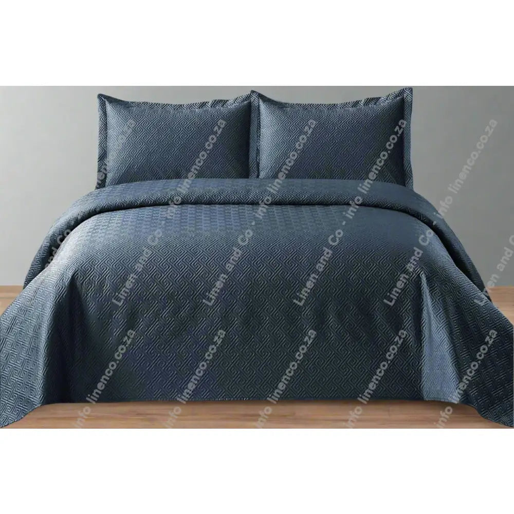 Denim Blue Rome Design Quilted Bedspread set on a bed.