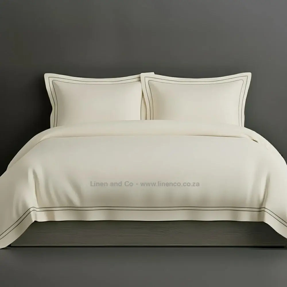 Cream percale duvet cover set with Oxford two-row white satin stitch border from Linen and Co, showcasing elegant hospitality bedding with subtle decorative detailing against a dark grey background.