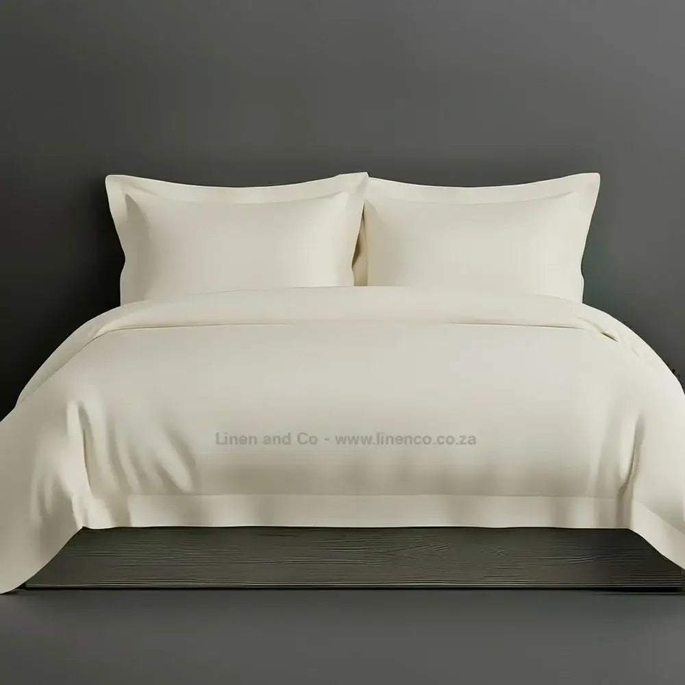 Cream percale duvet cover set with Oxford border from Linen and Co, showcasing elegant hospitality bedding with against a dark grey background.