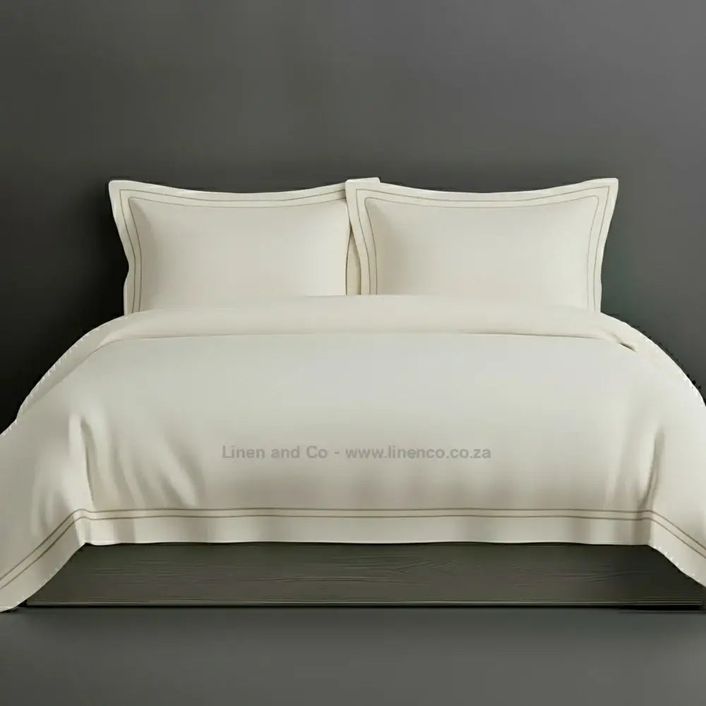 Cream percale duvet cover set with Oxford two-row white satin stitch border from Linen and Co, showcasing elegant hospitality bedding with subtle decorative detailing against a dark grey background.
