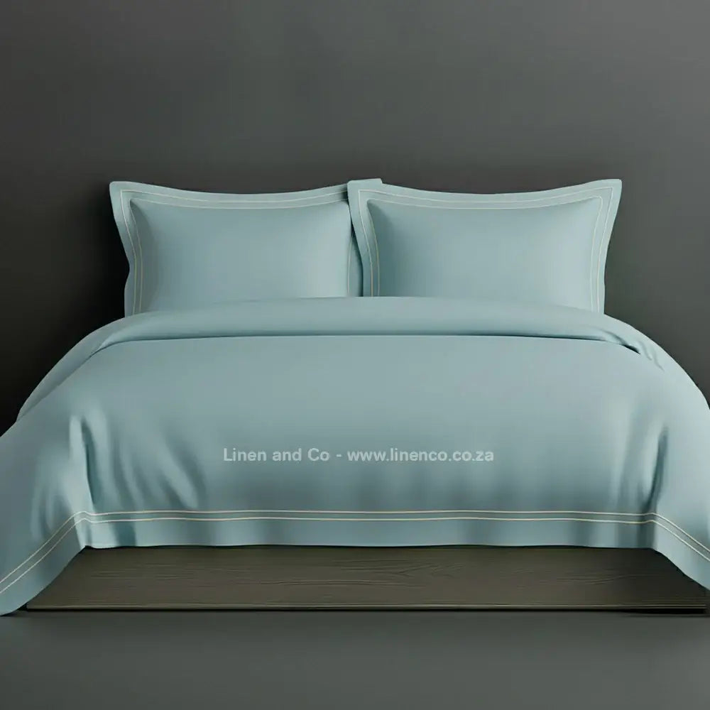 Duck egg percale duvet cover set with Oxford two-row white satin stitch border from Linen and Co, showcasing elegant hospitality bedding with subtle decorative detailing against a dark grey background.